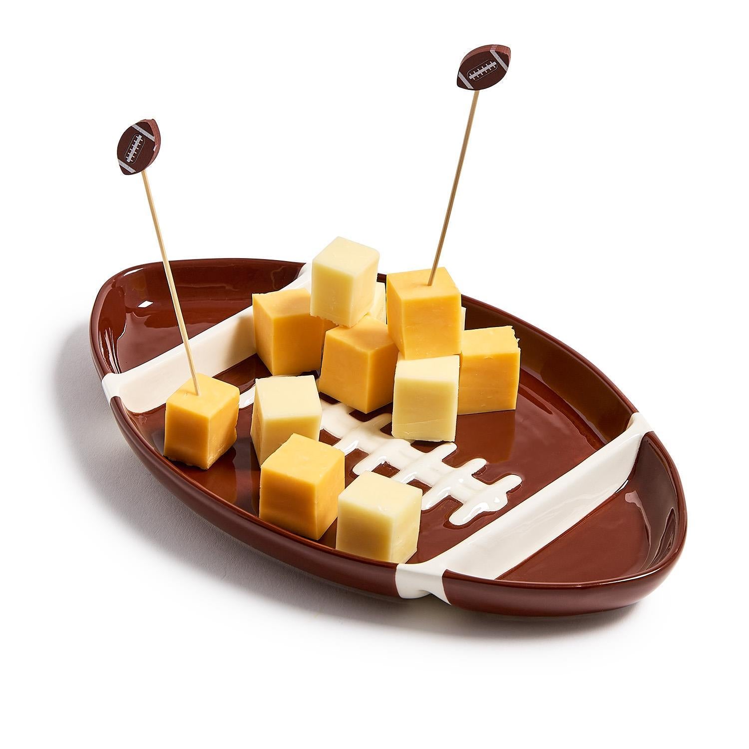 Football-shaped ceramic sectional serving platter with cheese cubes and football-themed toothpicks.