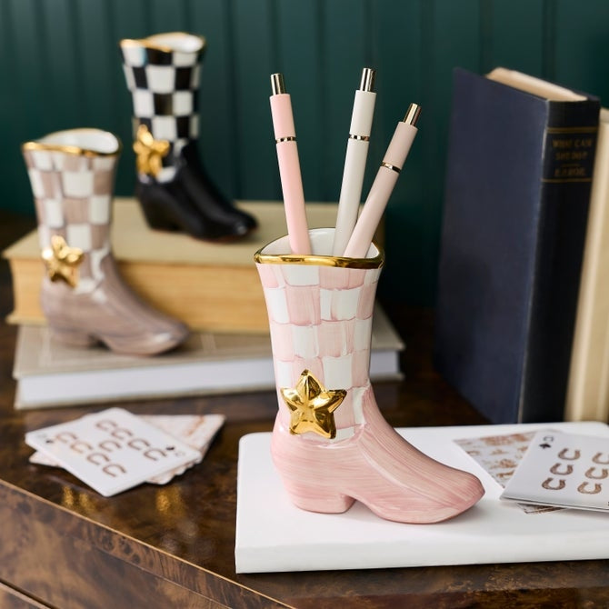 Pink and white checkered cowboy boot bud vase holding three pens on a white book.