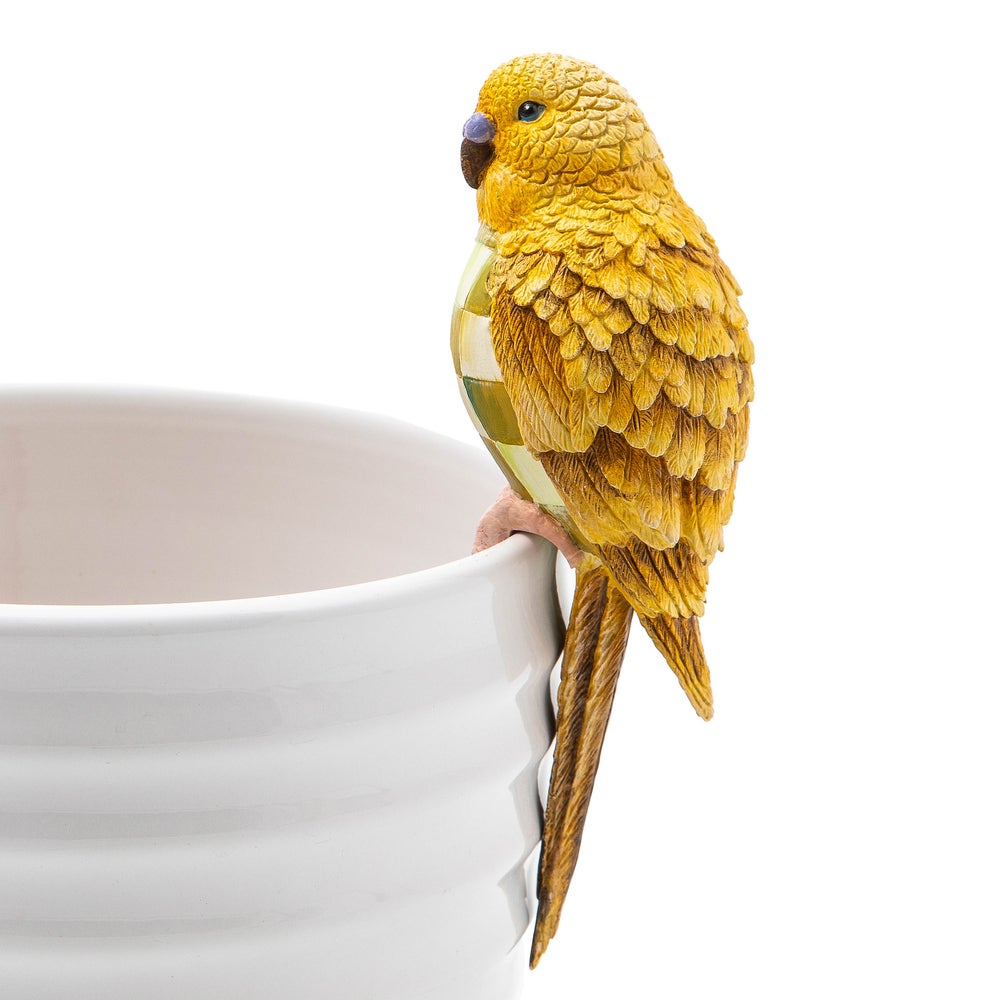 Chartreuse parakeet pot climber figurine made of resin perched on the edge of a white ceramic pot.