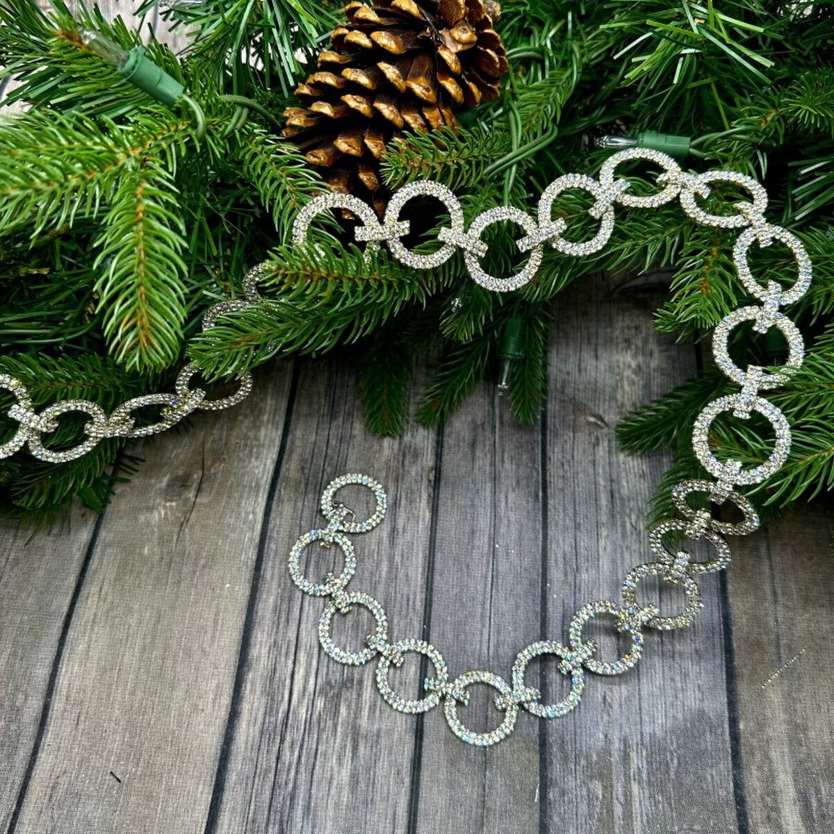 36-inch clear and silver circle crystal garland draped over pine branches on a wooden surface.