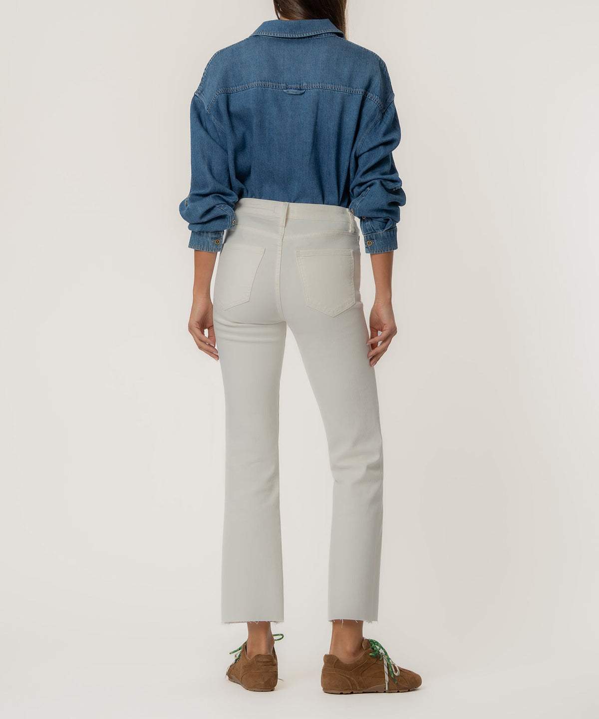 Rear view of a person wearing white high-rise ankle flare jeans with a raw hem and a denim shirt.