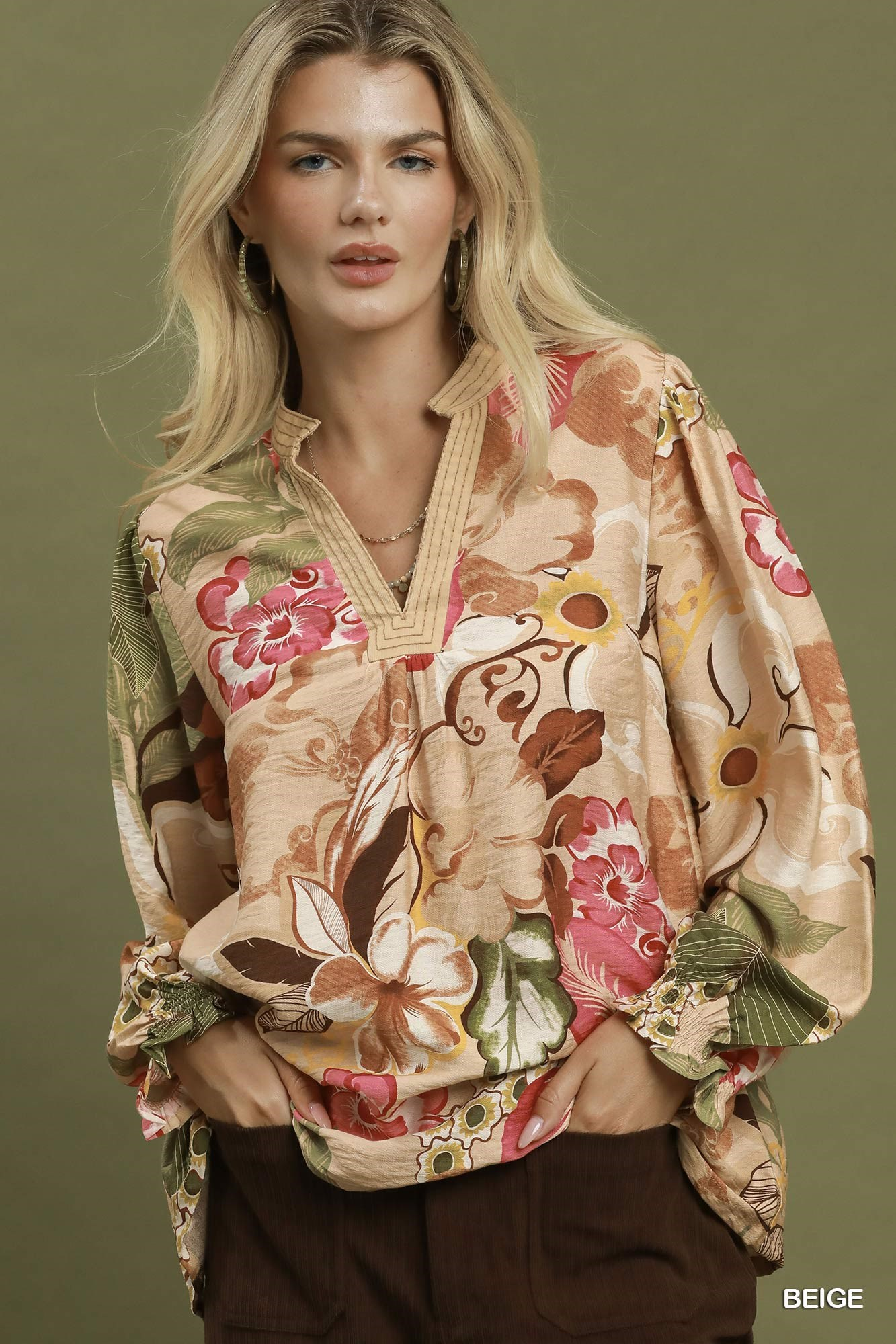 Woman wearing a Mia Floral Print V-Neck Blouse in beige with pink and green floral patterns.