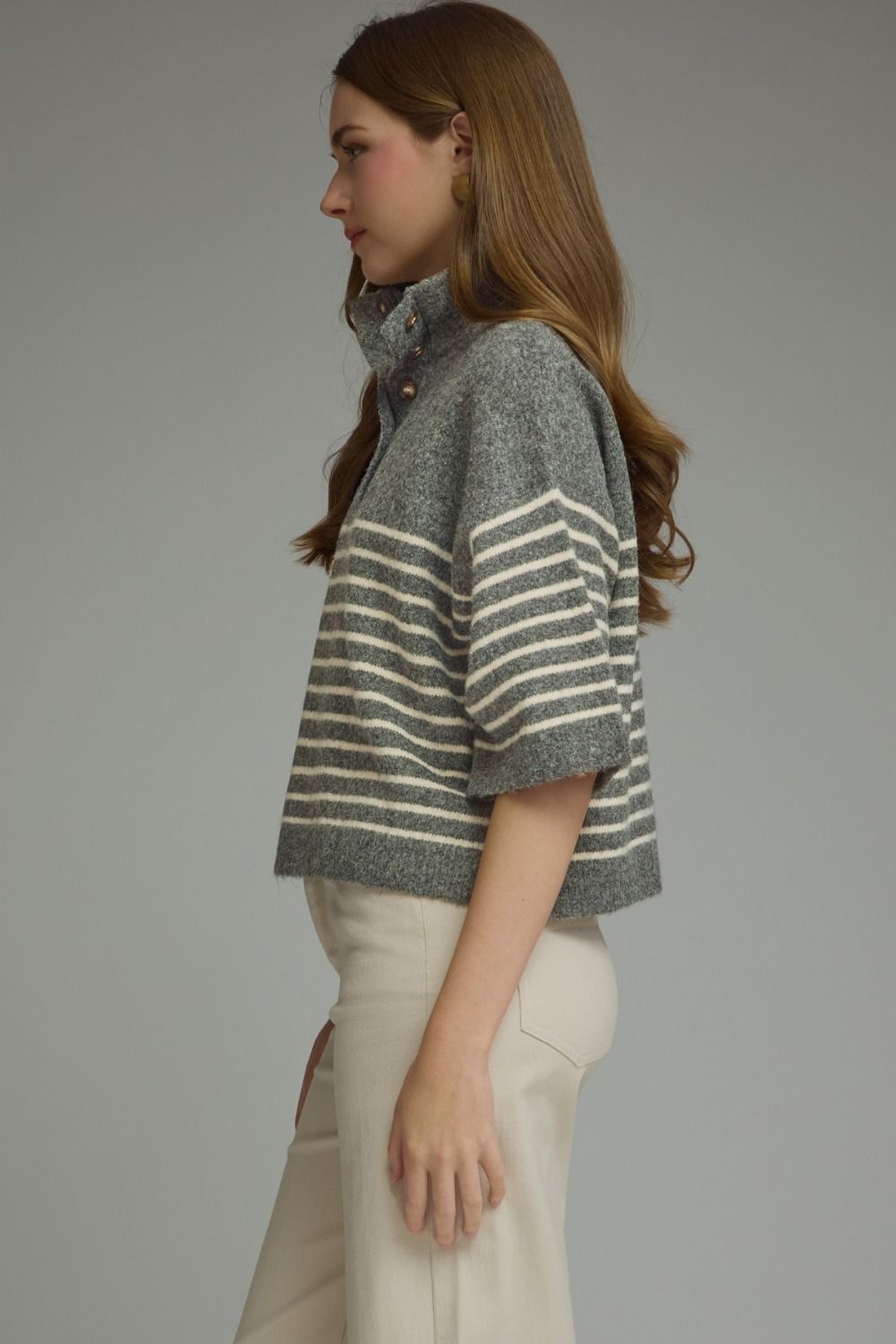 Side view of a woman wearing a grey and white striped short sleeve knit top with a high collar.