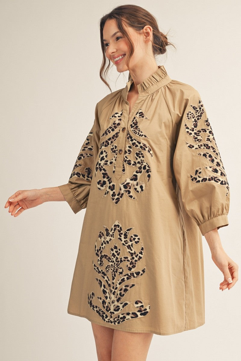Woman wearing a tan mini dress with leopard print baroque applique on the front and sleeves.