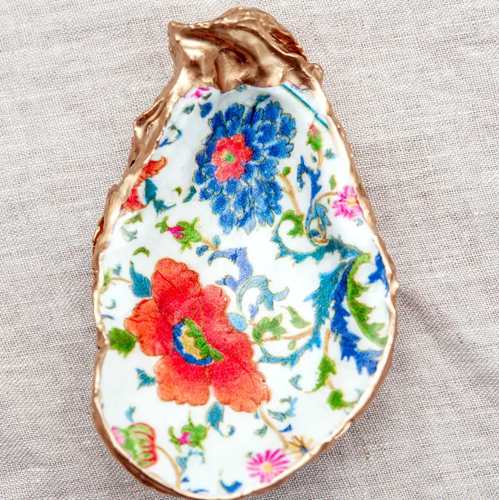 Decoupaged oyster shell with blue and red floral patterns and a metallic gold rim.
