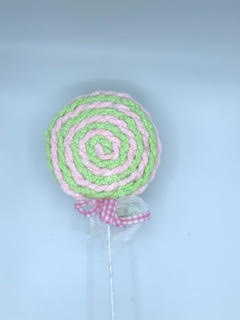 Pink and green fabric lollipop decoration with a spiral pattern and a gingham bow on the stem.