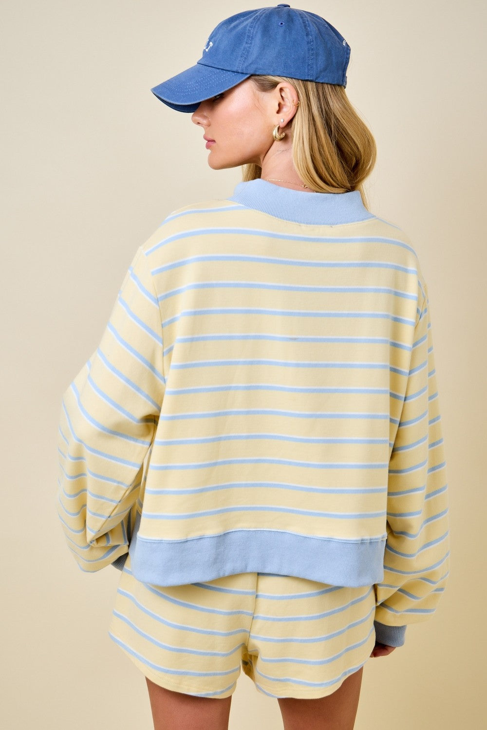 Back view of a woman wearing a yellow and blue striped mockneck sweatshirt and matching shorts.