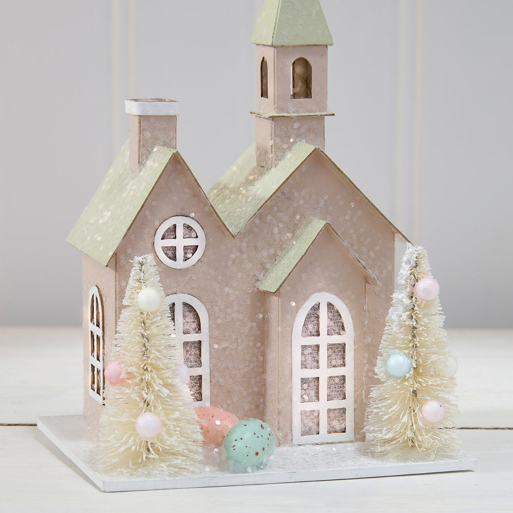 Cardboard Easter house with soft LED glow, sugared finish, and decorative trees.