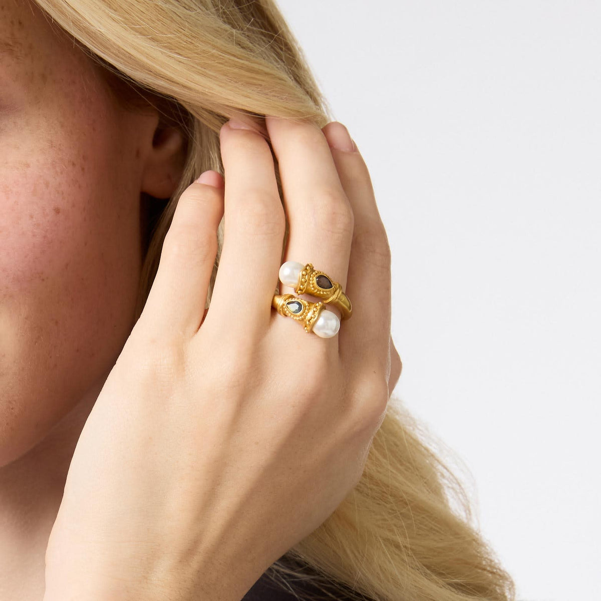 A person wearing the Baroque Demi Wrap Ring with two pearls and gold detailing on their ring finger.