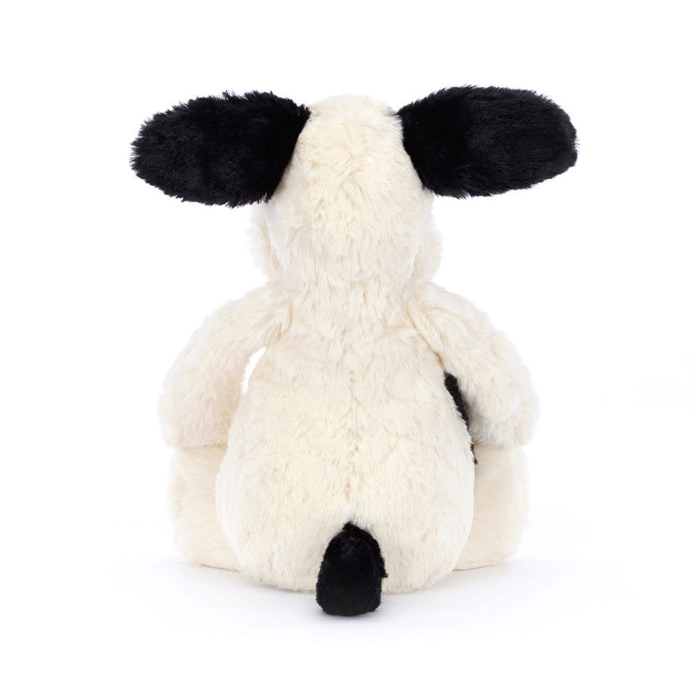 Sitting black and cream polyester puppy plush toy with smudgy facial markings.