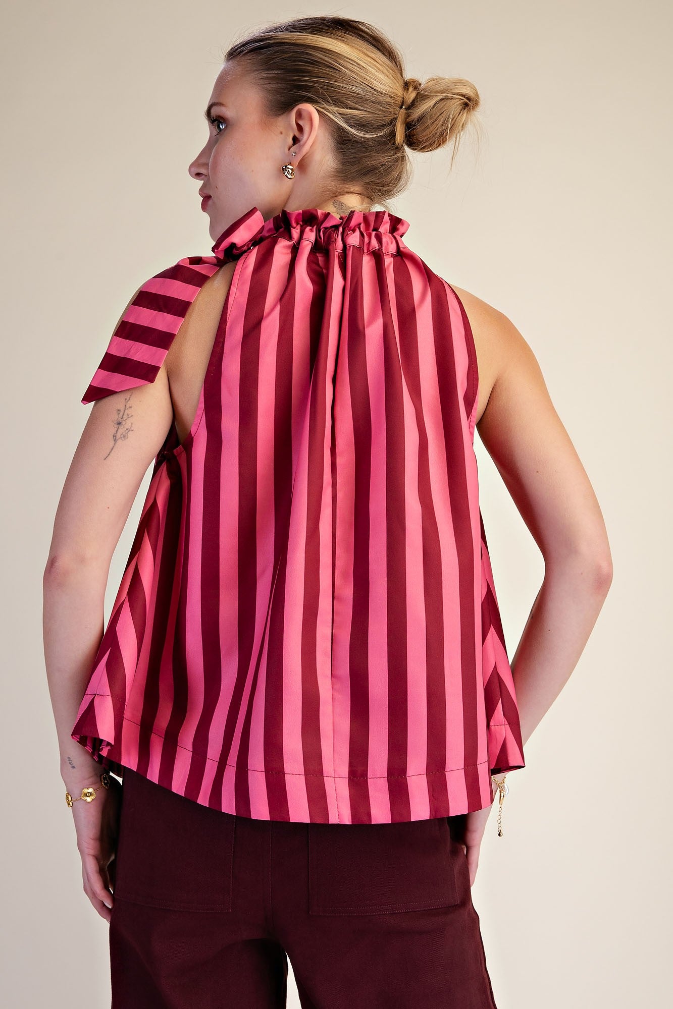 Back view of a woman wearing a pink and burgundy striped sleeveless top with a ruffled halter neck.