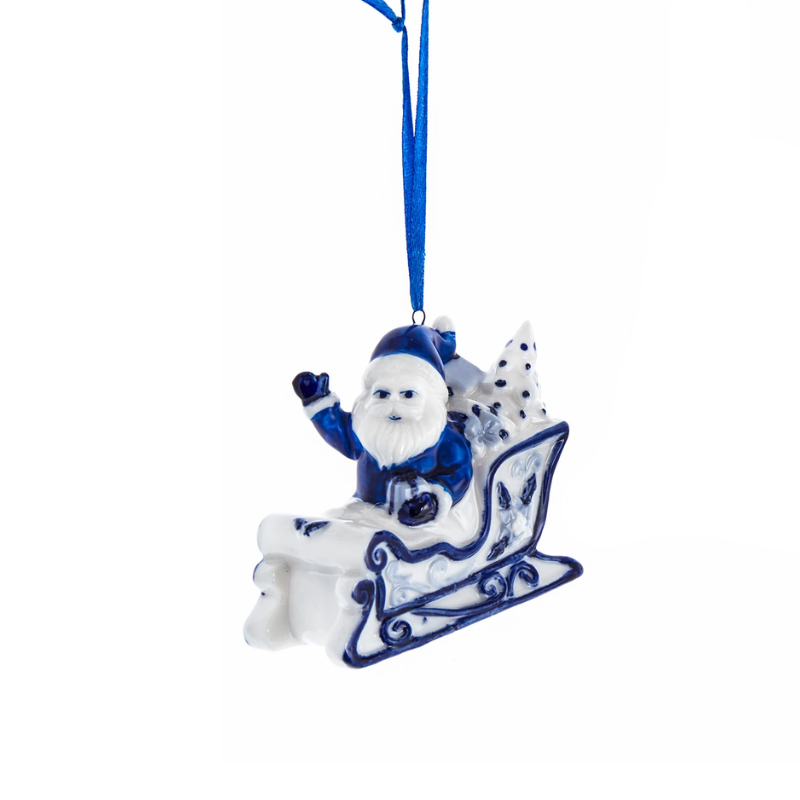 Blue and white ceramic Santa Claus ornament sitting in a sleigh with a blue ribbon hanger.