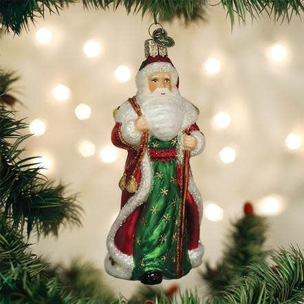 Father Christmas ornament with red coat holding golden bells against white background