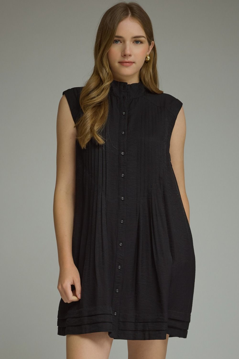 Model wearing Thea D31604 black sleeveless mini dress with high neck and pleated front detail.