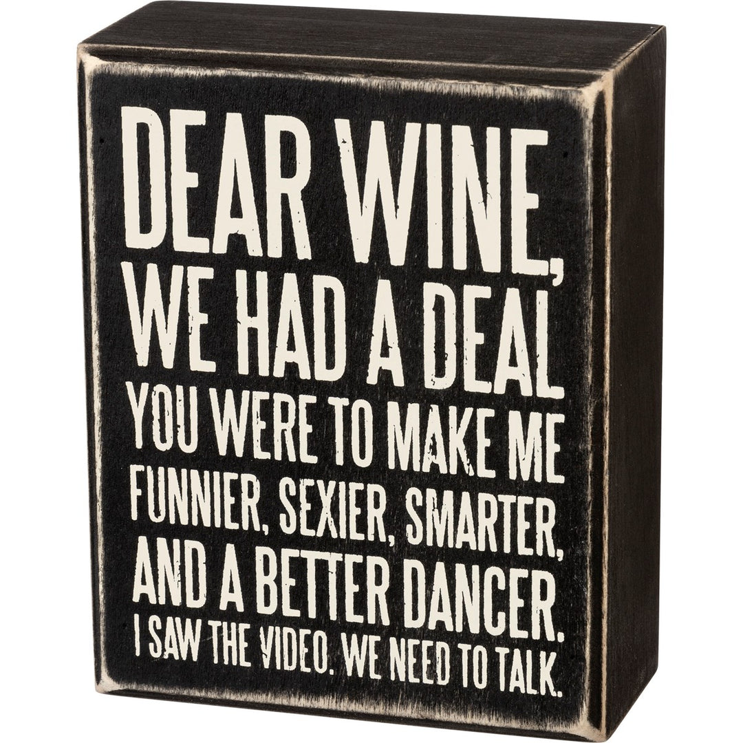Black wooden box sign with white text that reads 'Dear Wine, We Had A Deal. You Were To Make Me Funnier, Sexier, Smarter, And A Better Dancer. I Saw The Video. We Need To Talk.'