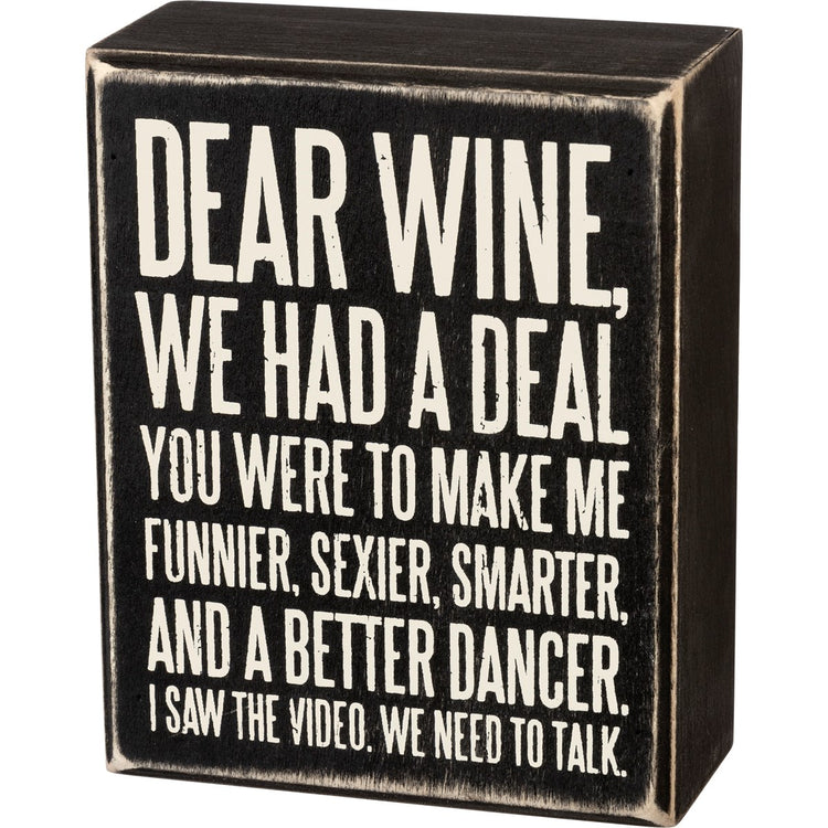 Black wooden box sign with white text that reads 'Dear Wine, We Had A Deal. You Were To Make Me Funnier, Sexier, Smarter, And A Better Dancer. I Saw The Video. We Need To Talk.'