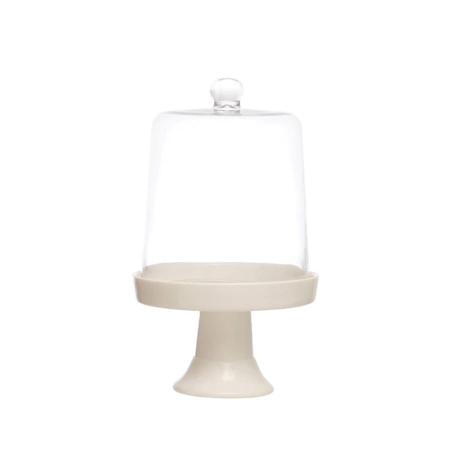 Cream ceramic cake stand with a tall clear glass cloche dome on a white background.