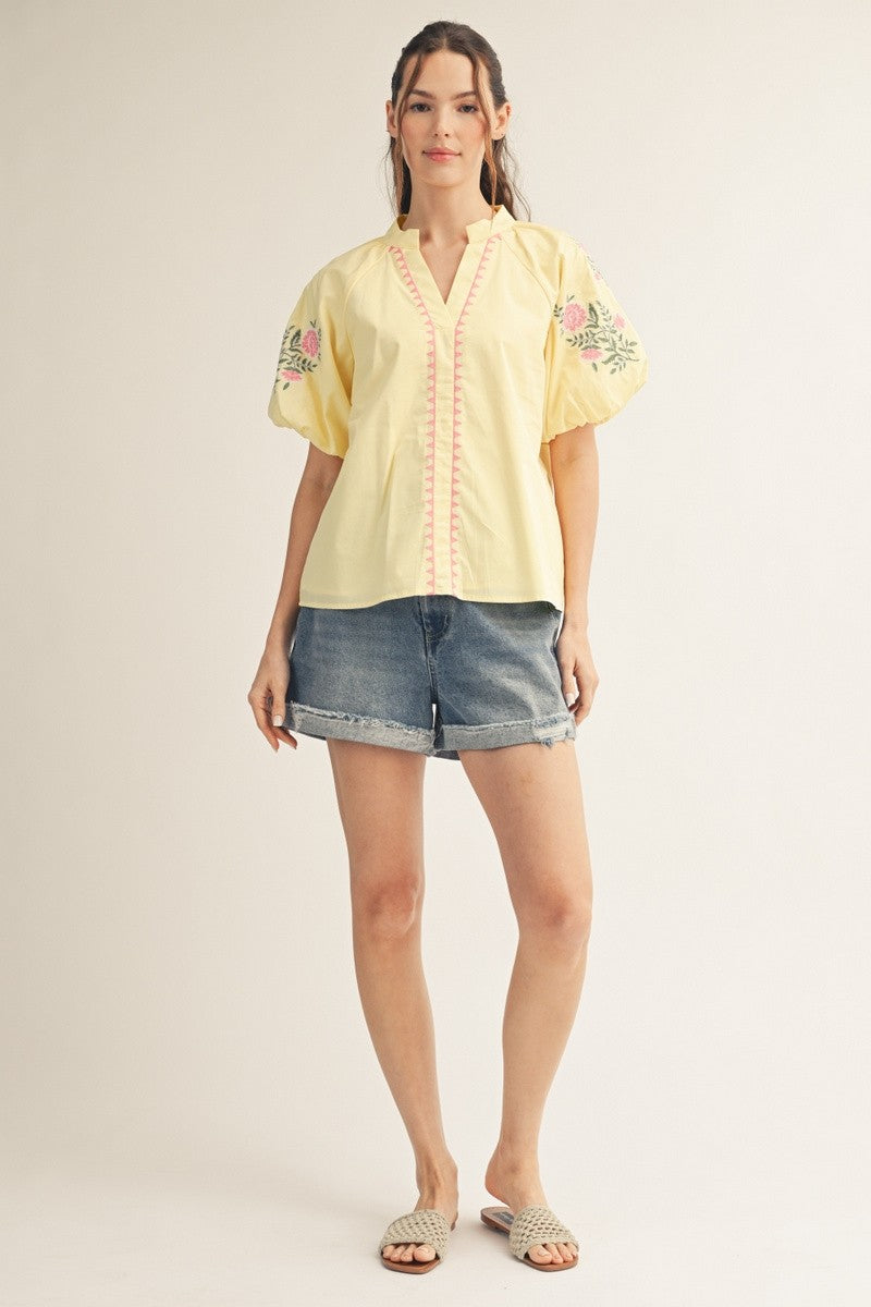 Woman wearing a Hailey yellow short puff sleeve V-neck top with pink floral embroidery and shorts.