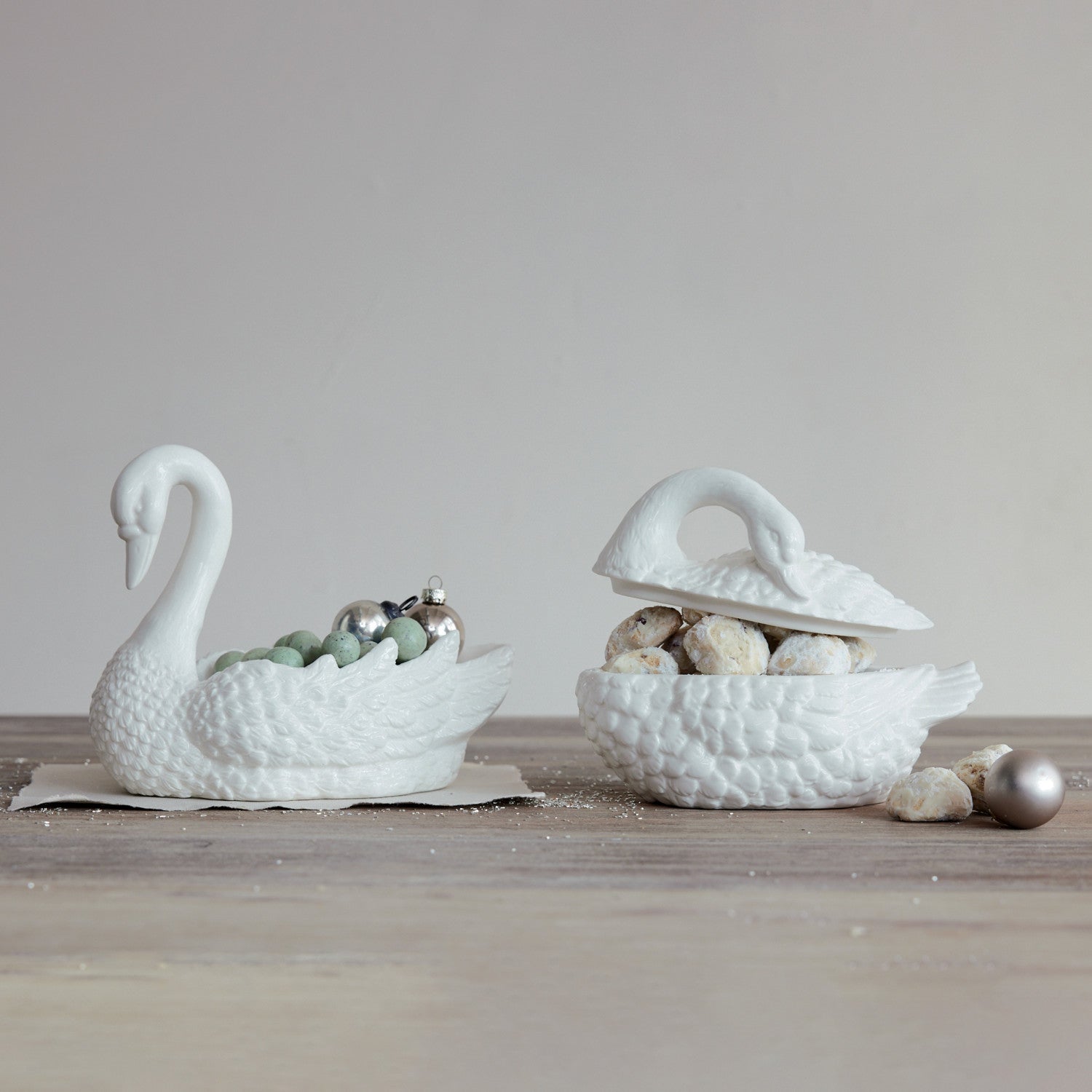 Two white stoneware swan-shaped dishes, one open and filled with cookies, on a wooden surface.