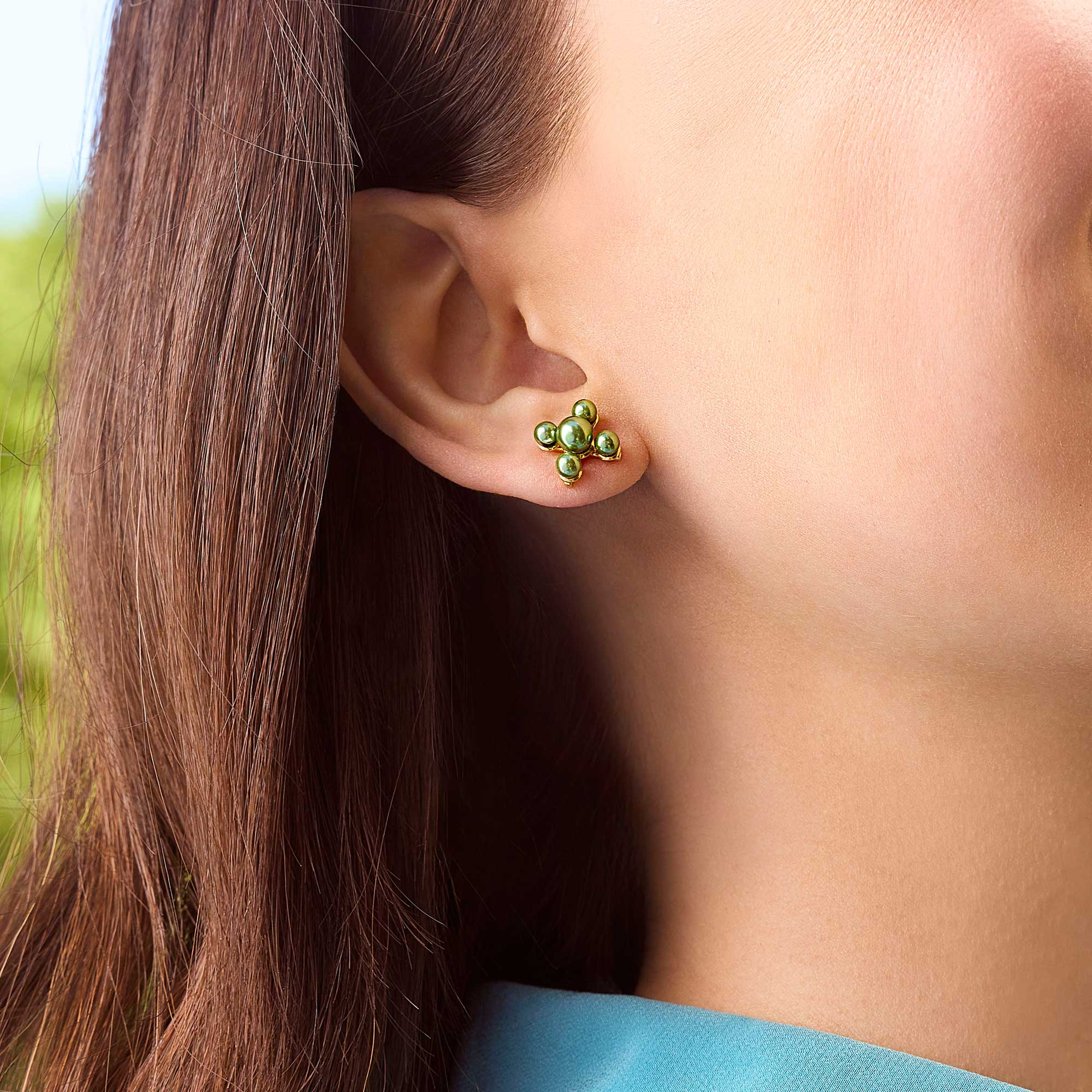 A person wearing a Millie Stud Emerald Pearl earring, featuring four green pearls in a gold setting.