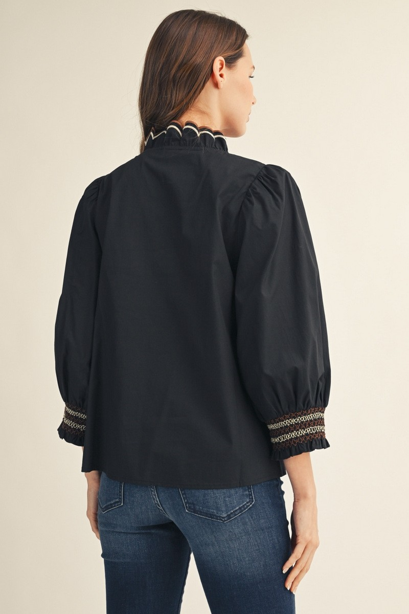 Back view of a woman wearing a black 3/4 puff sleeve top with embroidered smocking cuffs.