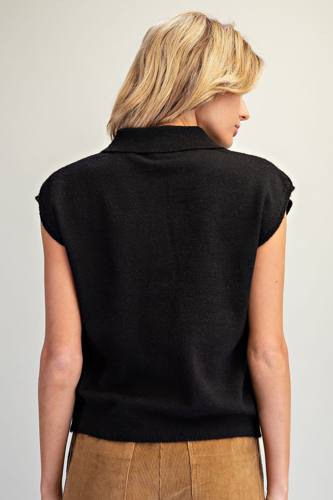 Back view of a woman wearing a black cap sleeve knit top with a polo collar and ribbed hem.