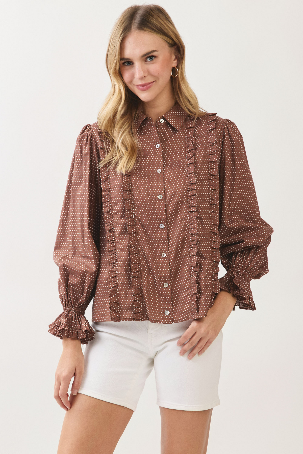 Woman wearing the Willa brown polka dot button-down shirt with ruffles and white shorts.