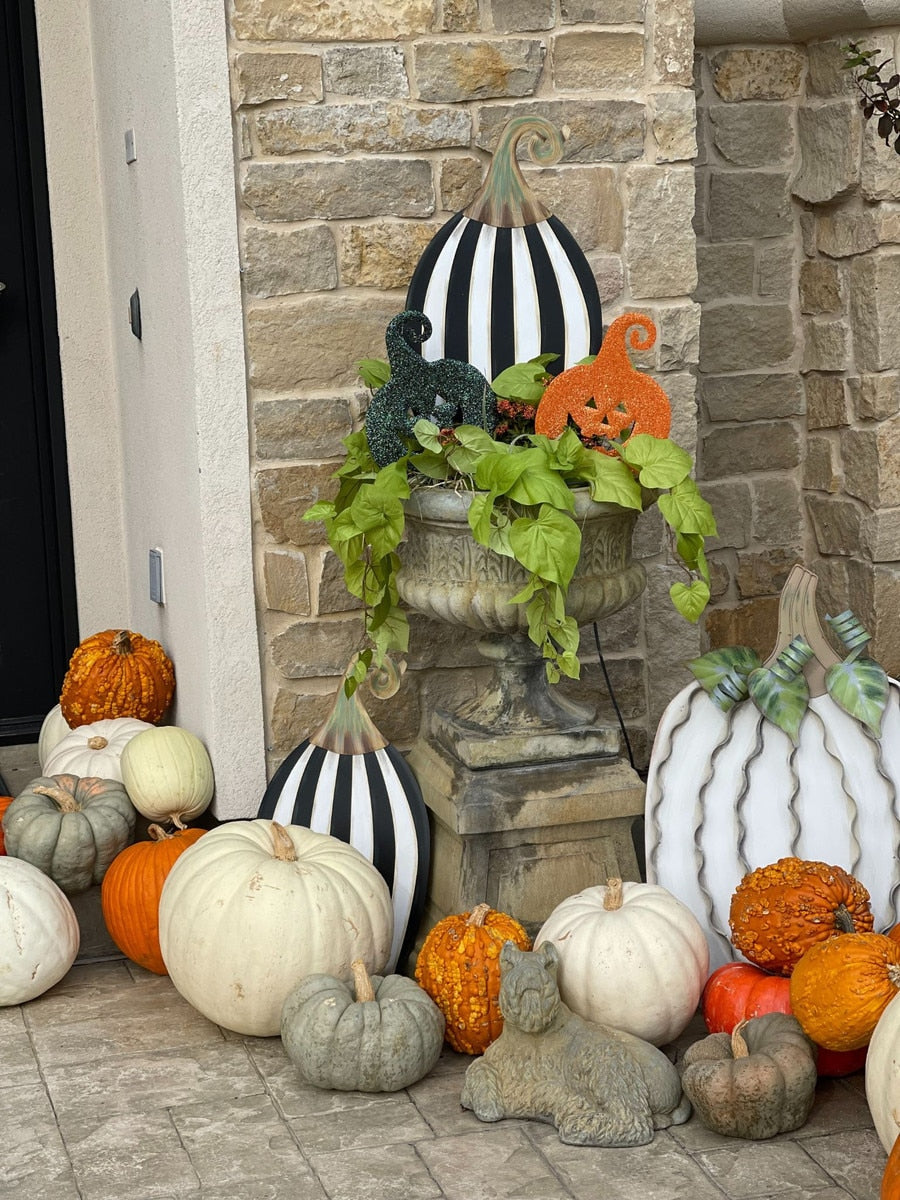 Tall black and white striped metal pumpkin yard stake displayed in an outdoor autumn arrangement.