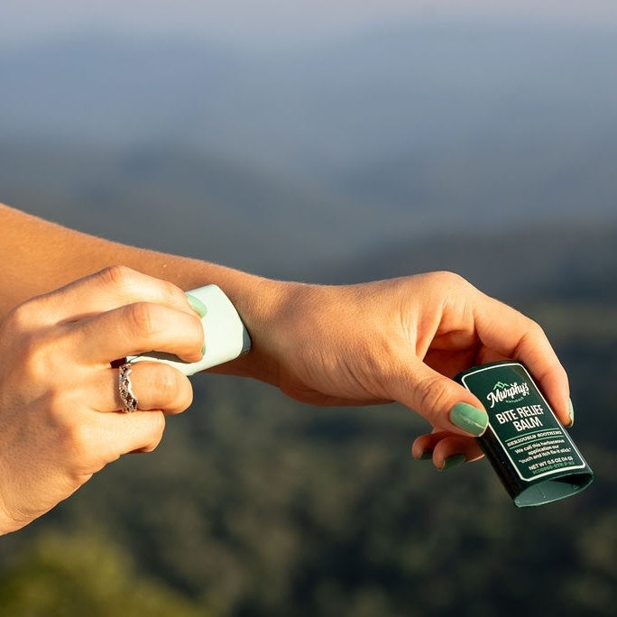 A white balm stick with a clear cap applied to skin near an insect bite.