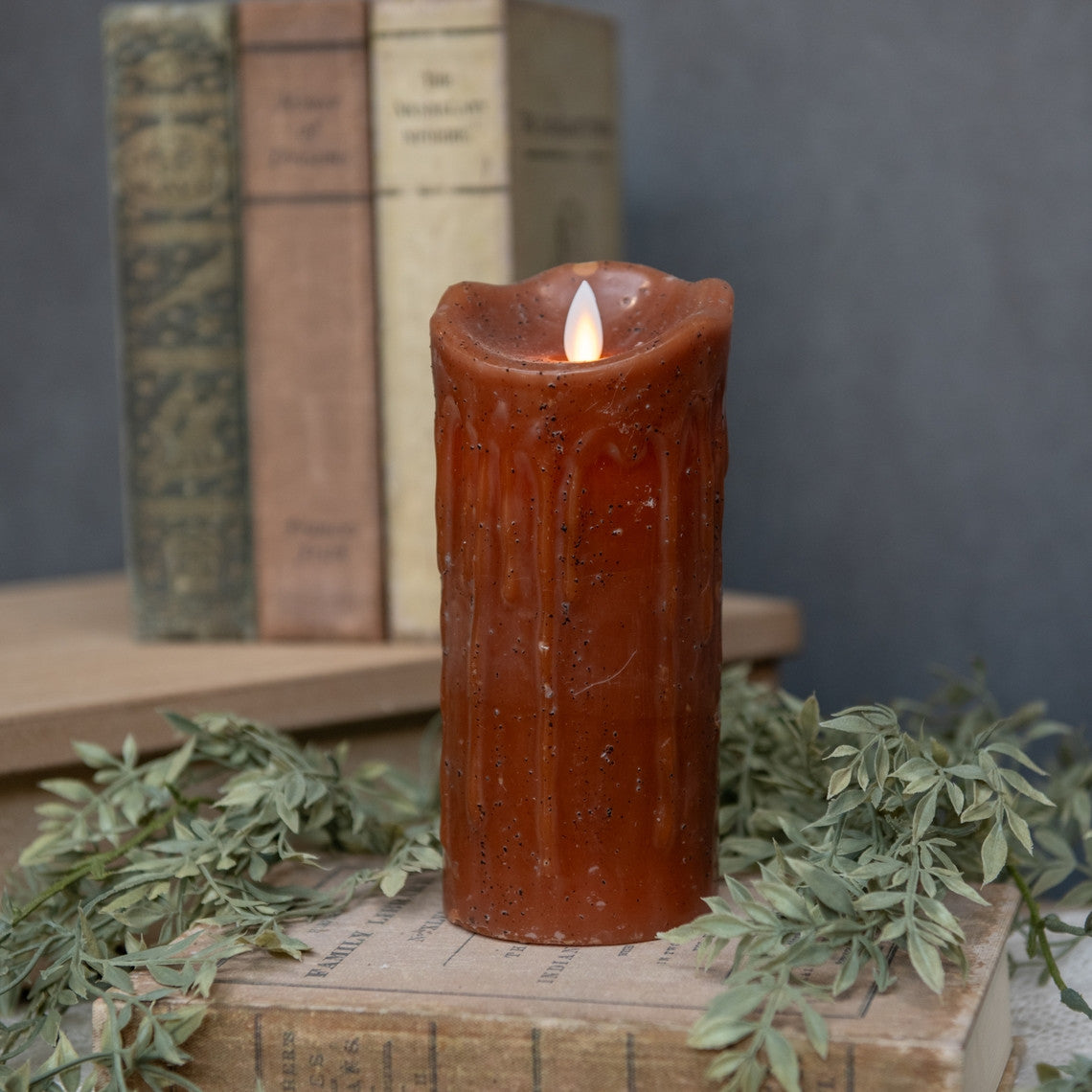 Moving Flame Bronze Pillar Candle with a flickering LED flame on a stack of vintage books.