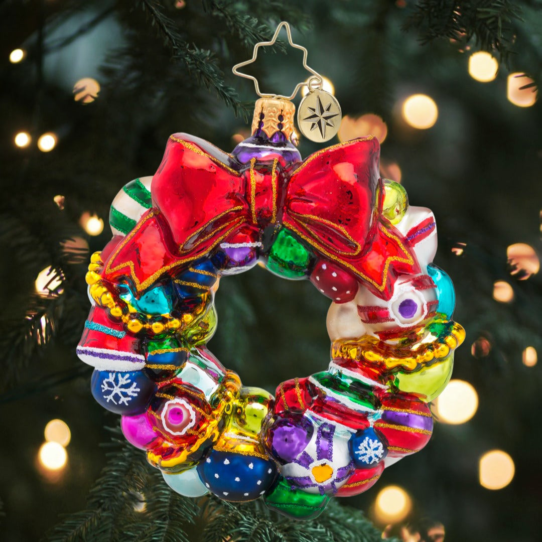 Colorful glass wreath ornament with a large red bow, rounds, and reflectors on a Christmas tree.