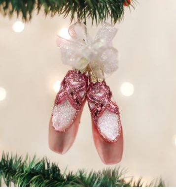 Pink glittery ballet slipper Christmas ornament with a white ribbon bow hanging on a tree.