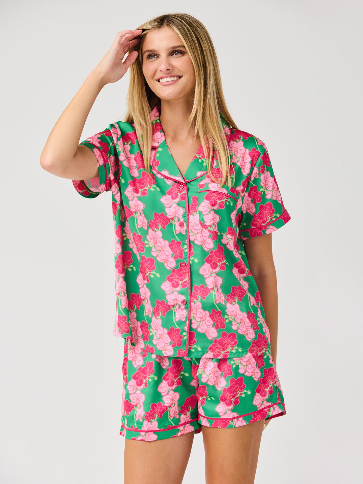 Woman wearing a green and pink floral satin short-sleeve pajama set with button-front top.