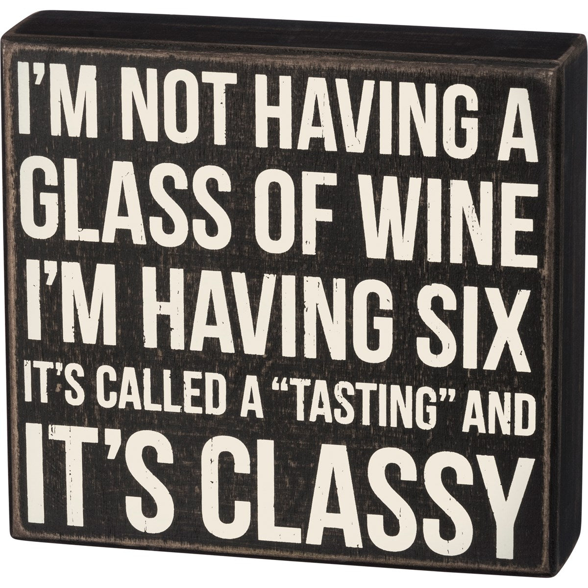 Black wooden box sign with white text reading 'I'M NOT HAVING A GLASS OF WINE I'M HAVING SIX IT'S CALLED A "TASTING" AND IT'S CLASSY'.