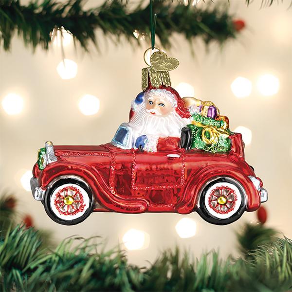 Santa Claus in a red antique car glass ornament with gifts, hanging on a Christmas tree.