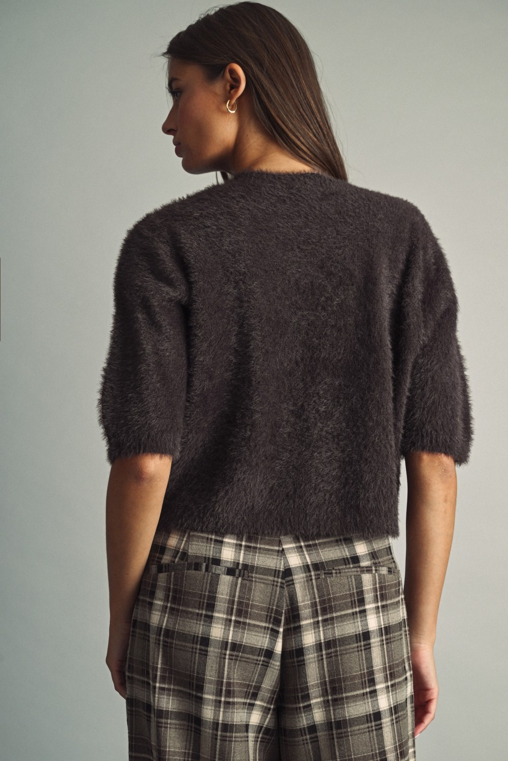 Back view of a woman wearing a chocolate brown fluffy faux-fur cropped sweater and plaid trousers.