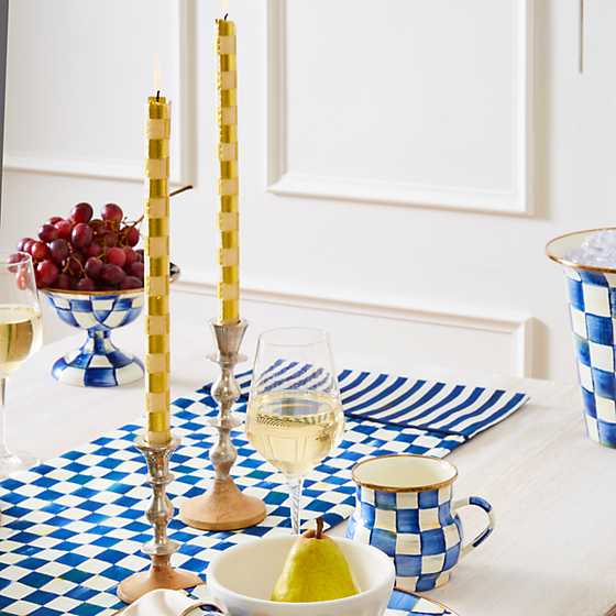 Two gold and ivory checkered dinner candles in silver holders on a blue and white table runner.