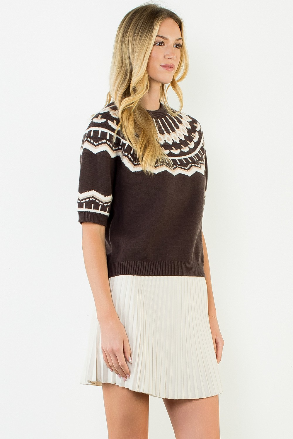 Woman wearing the Nicole Short Sleeve Pattern Sweater in brown with a white pleated skirt.