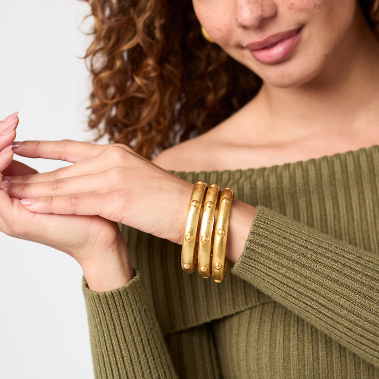A person wearing three thick, gold-toned Solara Bangles with raised stud details on their wrist.