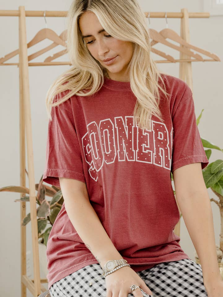 Woman wearing a red Athena OU Sooners Polka Dot Puff Ink CC Tee with white arched lettering.
