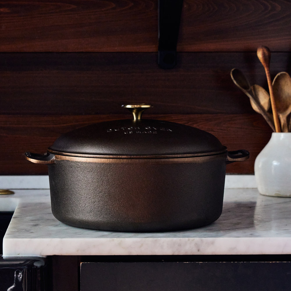 7.25 QT cast iron Dutch oven with a domed lid and gold-toned knob on a marble countertop.