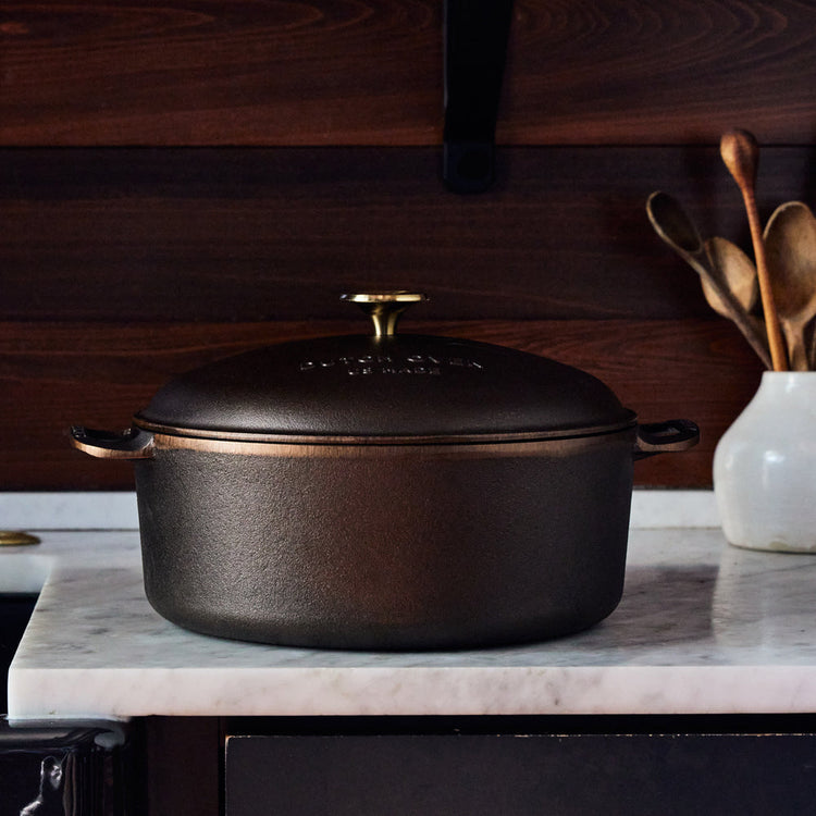 7.25 QT cast iron Dutch oven with a domed lid and gold-toned knob on a marble countertop.