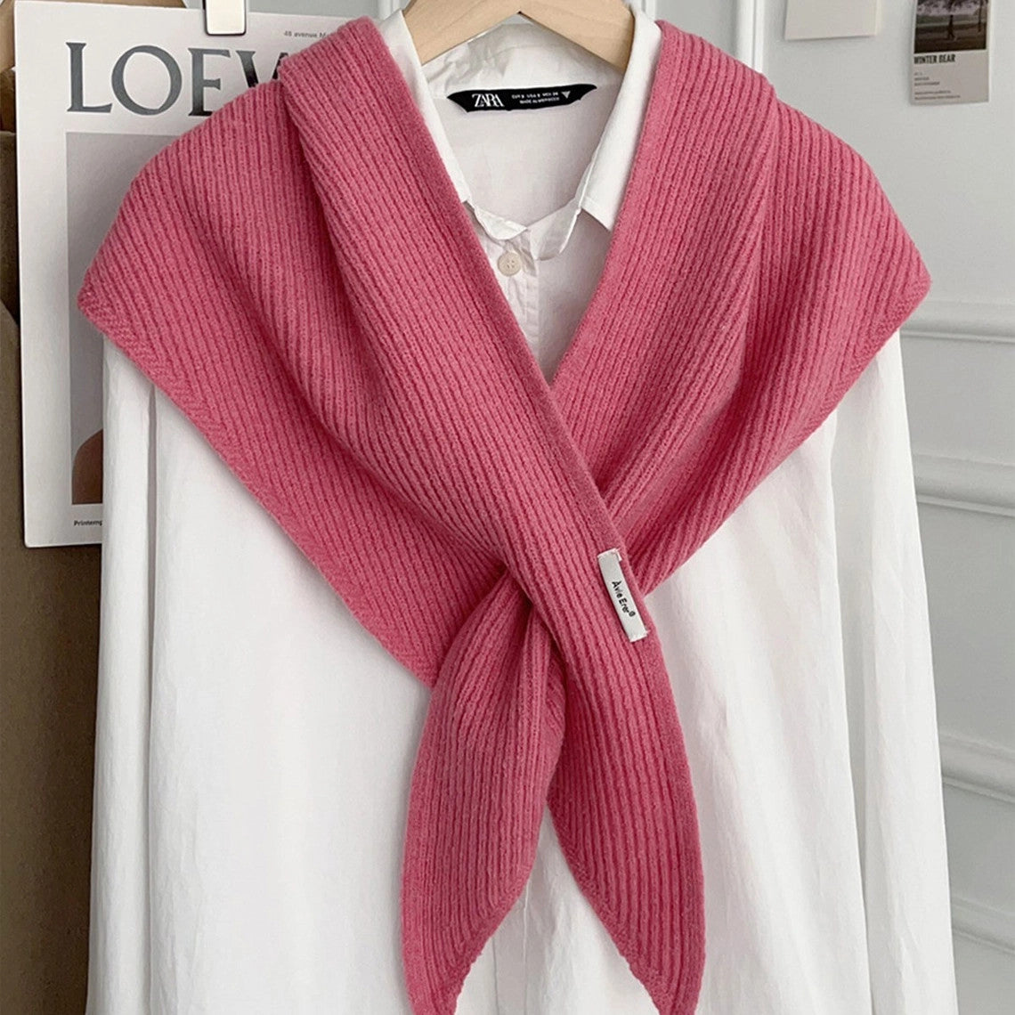 Pink knitted solid cross triangle shawl draped over a white button-down shirt on a hanger.