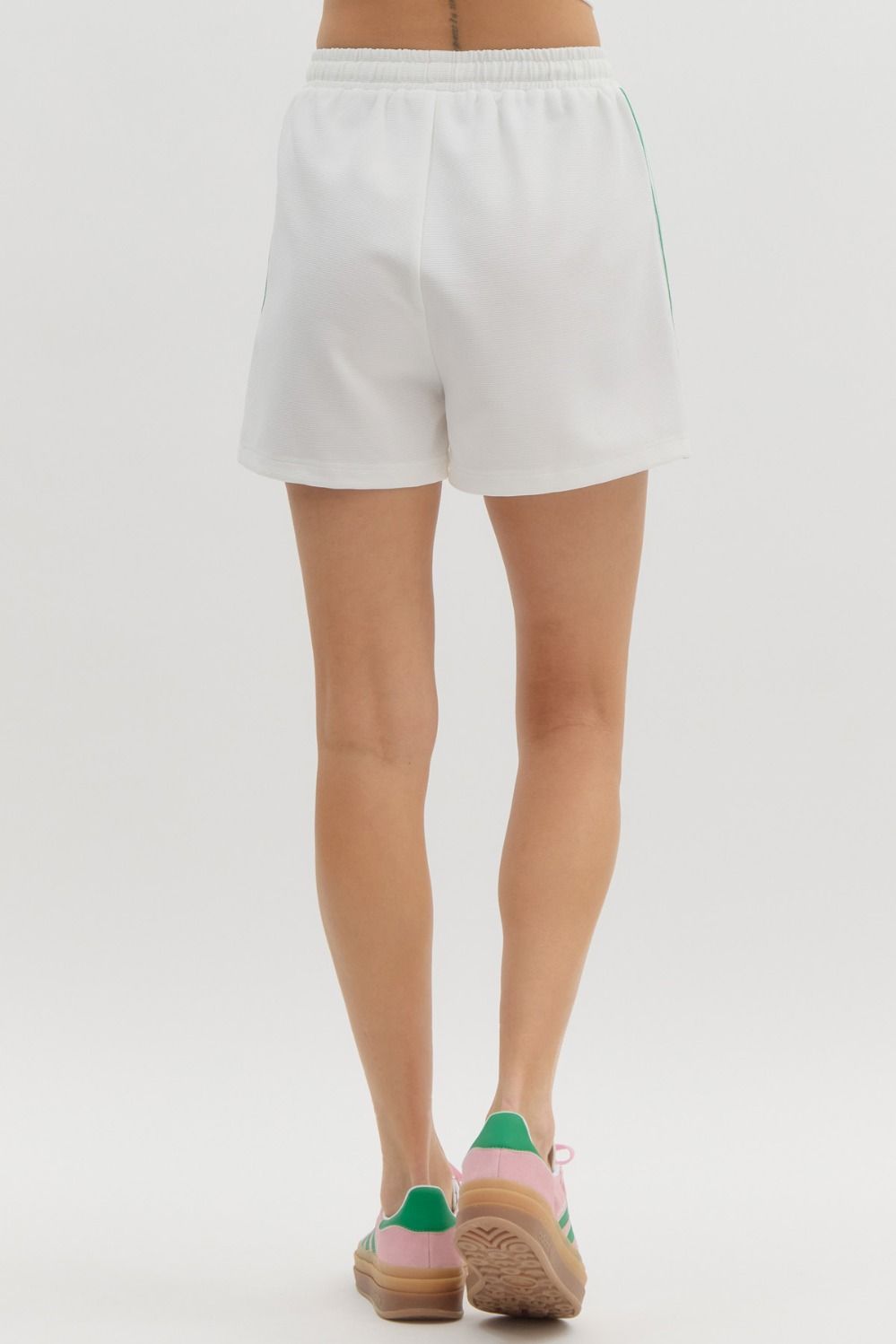 Rear view of a person wearing white Jasmine Jersey Knit Shorts with green side stripes.