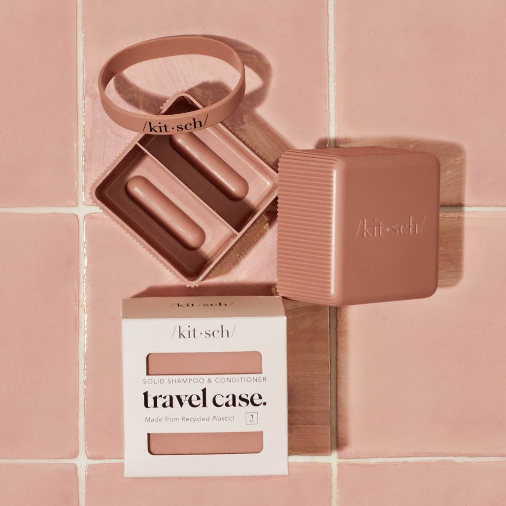 Compact recycled plastic travel case with removable silicone band closure and internal divider holding two solid shampoo bars.