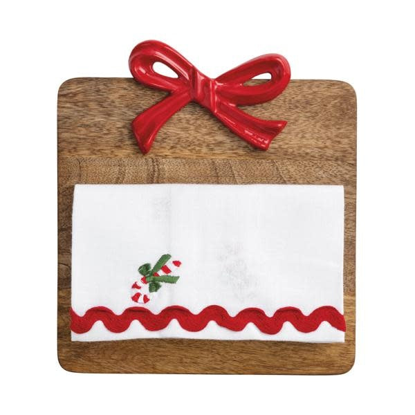 Square mango wood serving board with cast aluminum bow handle paired with embroidered cotton towel featuring ric-rac trim.