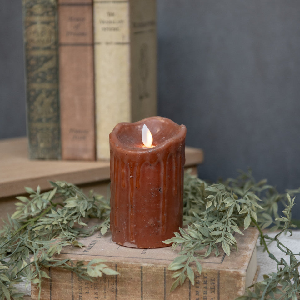Moving Flame Bronze Pillar Candle with a flickering LED flame on a stack of vintage books.