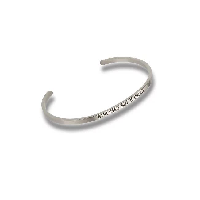 Silver-toned metal cuff bracelet engraved with the text STRESSED BUT BLESSED.