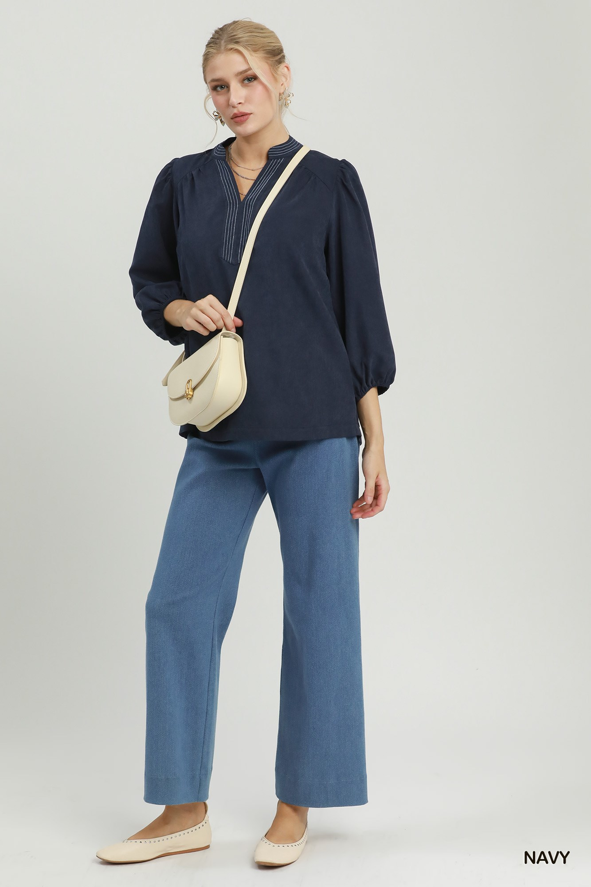 Woman wearing a navy Clara Sueded Split Neck Blouse with contrast stitching and blue trousers.