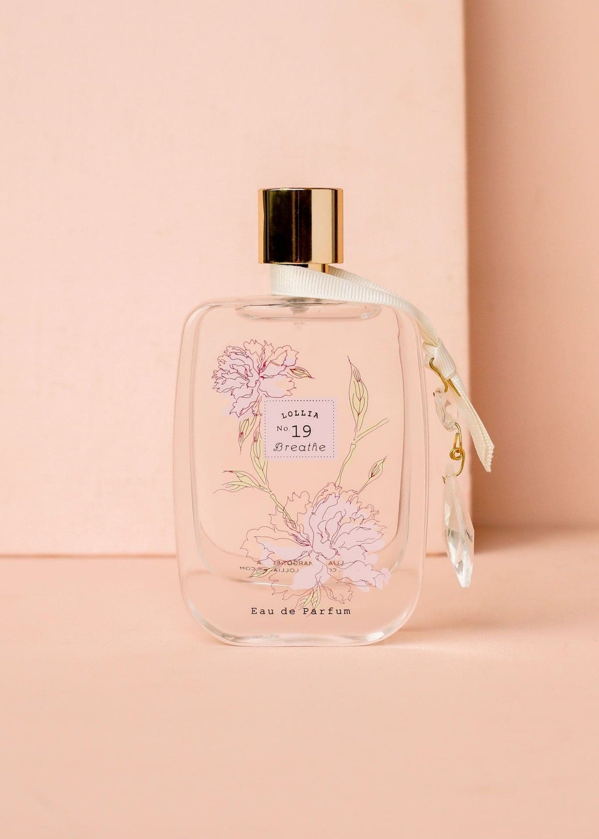 Glass perfume bottle with gold accents featuring floating peony flowers and a satin crystal tie.